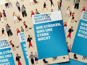 Flyer der Partnerschaft für Demokratie Landkreis Sankt Wendel liegen kreuz und quer auf einem Tisch.