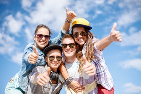 Vier Personen mit Sonnenbrillen recken die Daumen hoch und lächeln. 